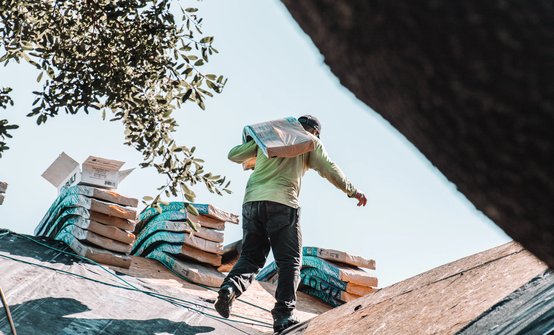 A roofer carrying a bundle of shingles across a roof